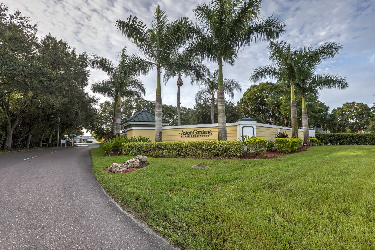 A landscaped entrance with palm trees and a building in a tropical setting.