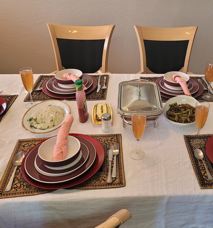 A well-arranged dining table set for a meal, featuring plates, cutlery, glasses, and pink folded napkins on a white tablecloth.