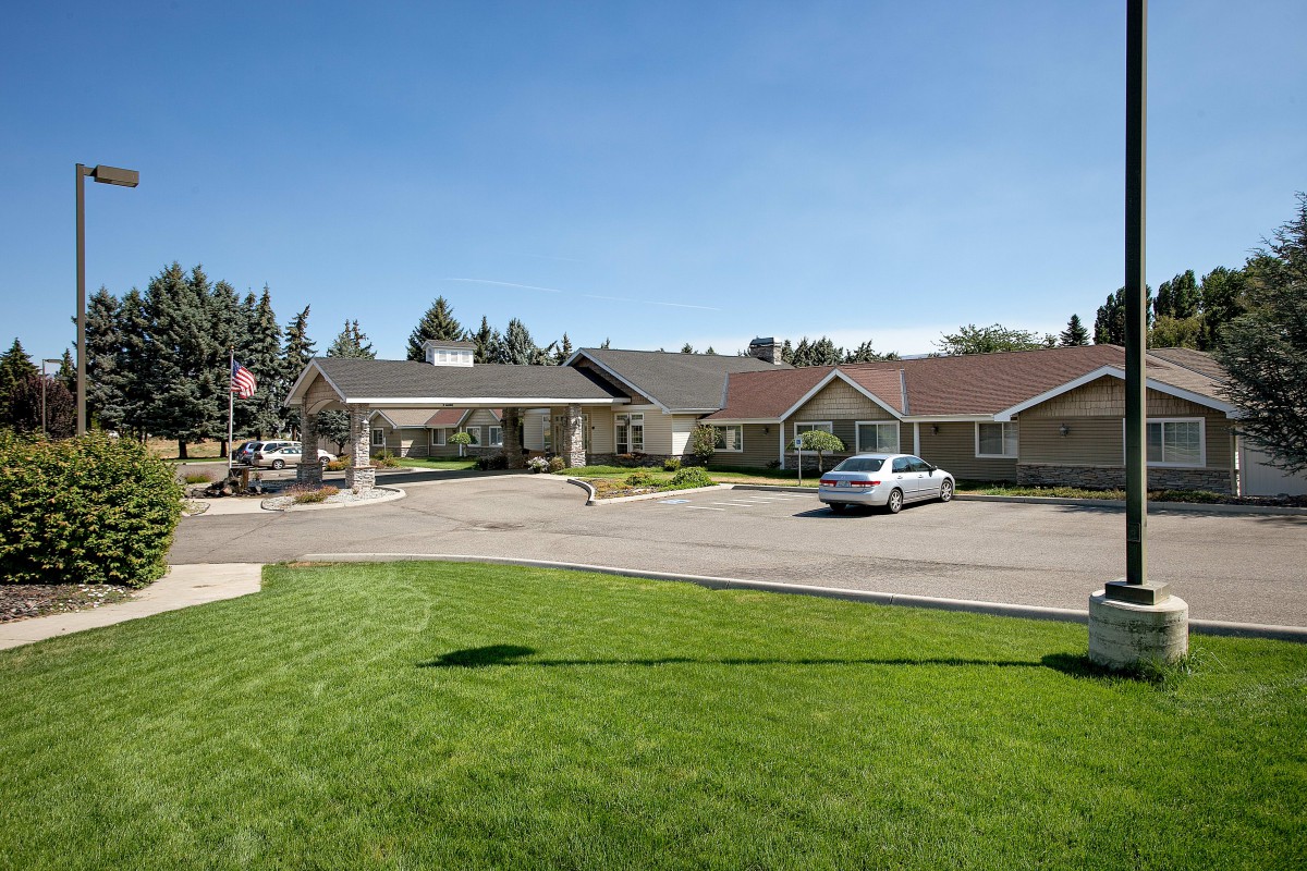 A building with a parking lot and landscaped lawn under a clear blue sky.