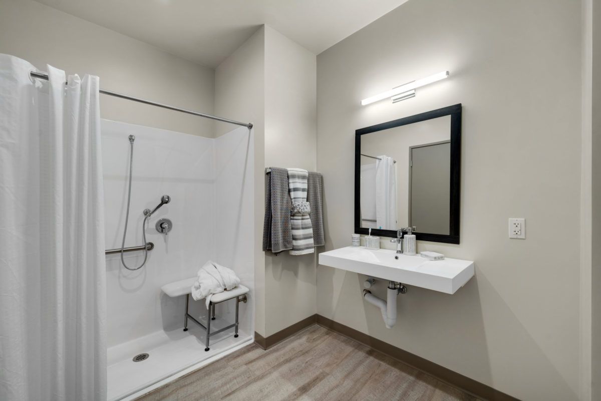 A modern bathroom with a walk-in shower, wall-mounted sink, and large mirror.