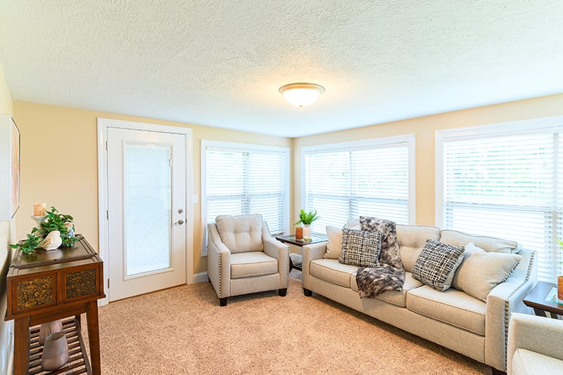 A bright and cozy living room with a sofa, armchair, and large windows allowing natural light.