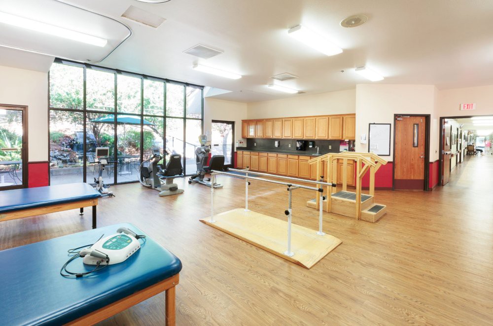 A well-equipped rehabilitation room with exercise equipment and parallel bars for physical therapy.
