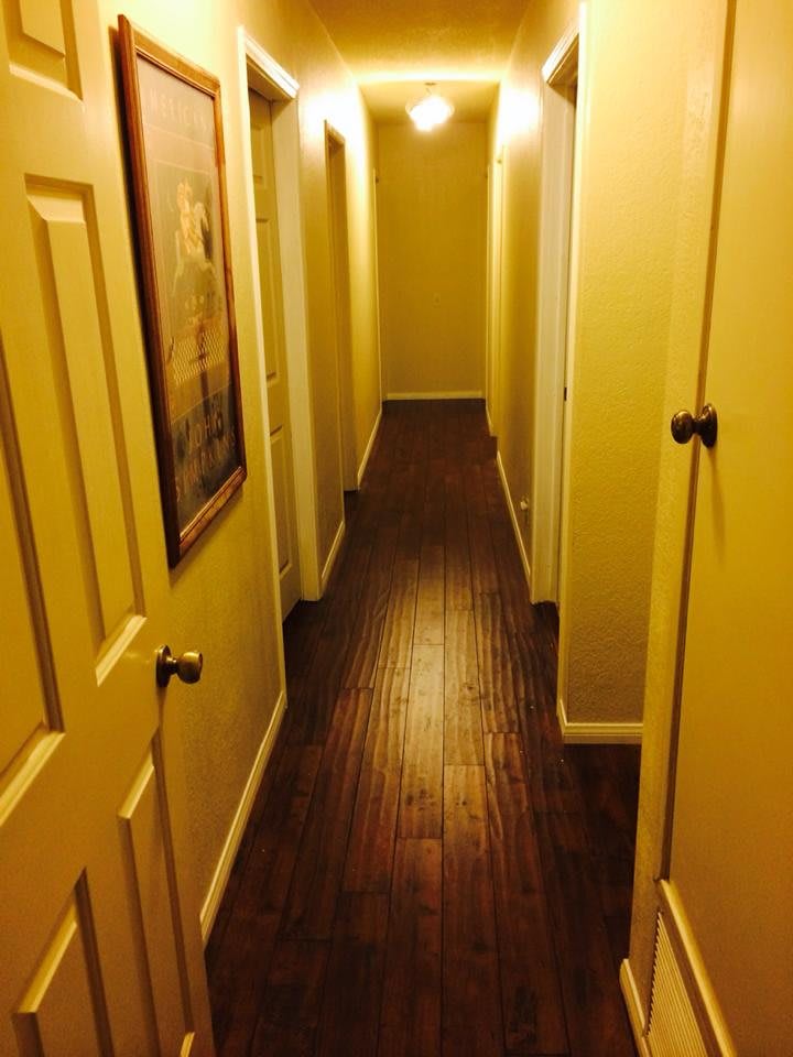 A dimly lit hallway with yellow walls and multiple doors on each side, featuring a wooden floor.