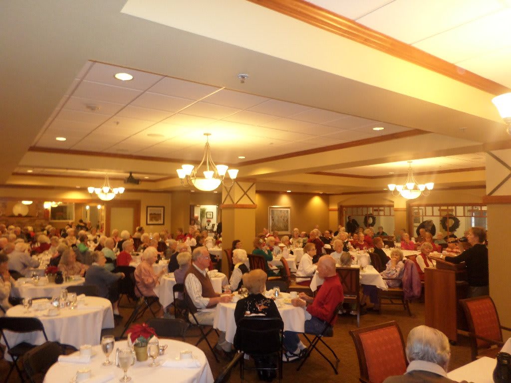 A large group of people enjoying a meal at a community event in a dining room setting.