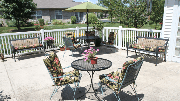 A cozy patio with colorful chairs and an umbrella, surrounded by a white fence and potted plants.