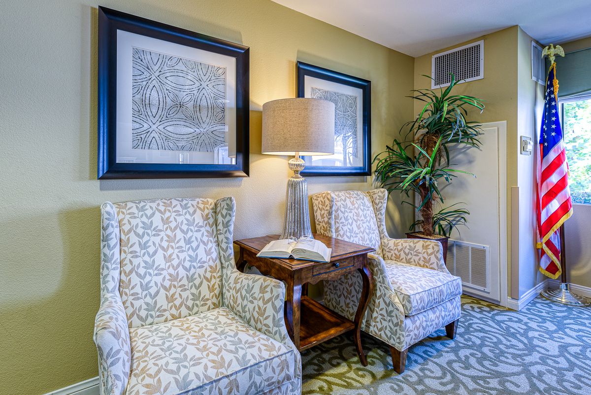 A cozy living room corner with patterned chairs, a lamp, and framed artwork.