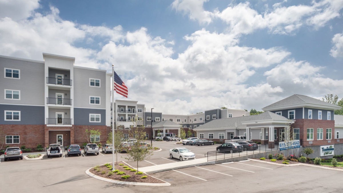 A modern building complex with an adjacent parking lot and an American flag flying under a partly cloudy sky.