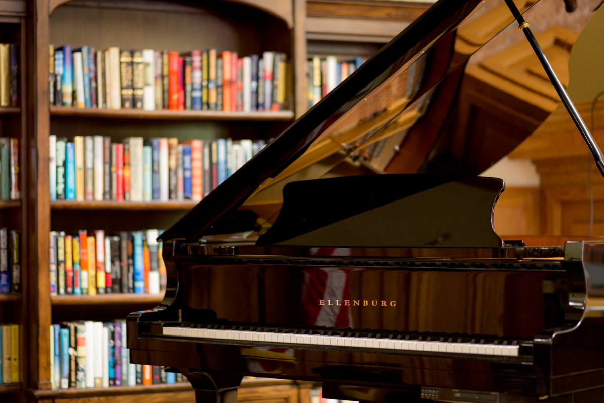 A grand piano in front of a bookshelf filled with books.