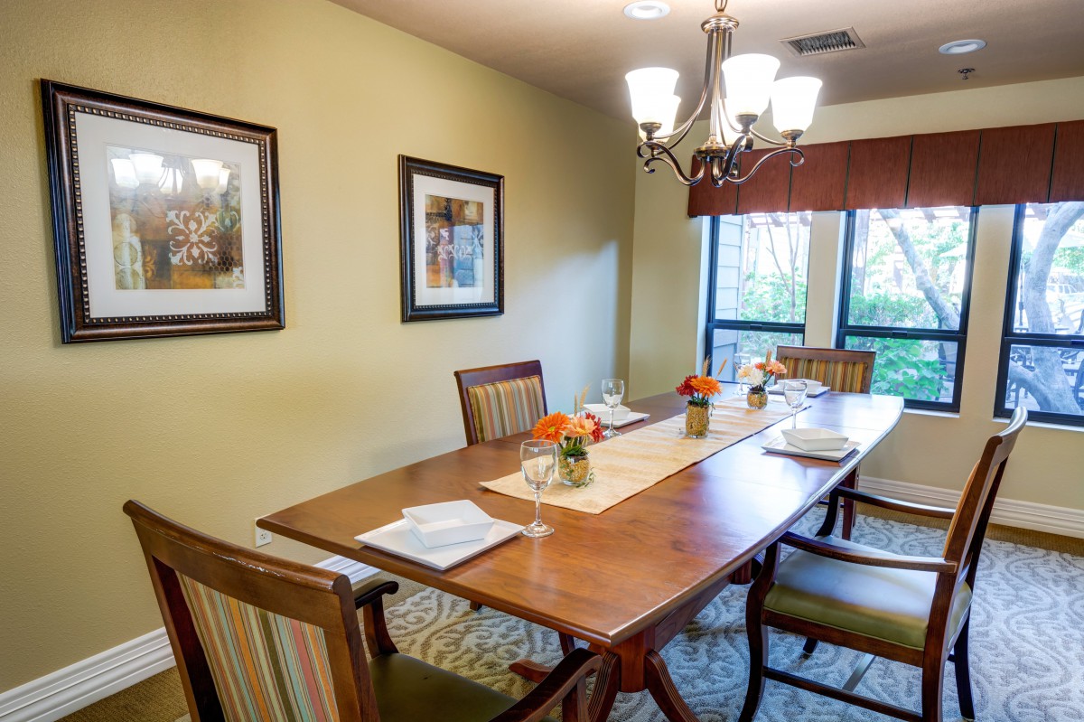 A well-lit dining room with a wooden table and chairs, decorated with artwork and flowers.