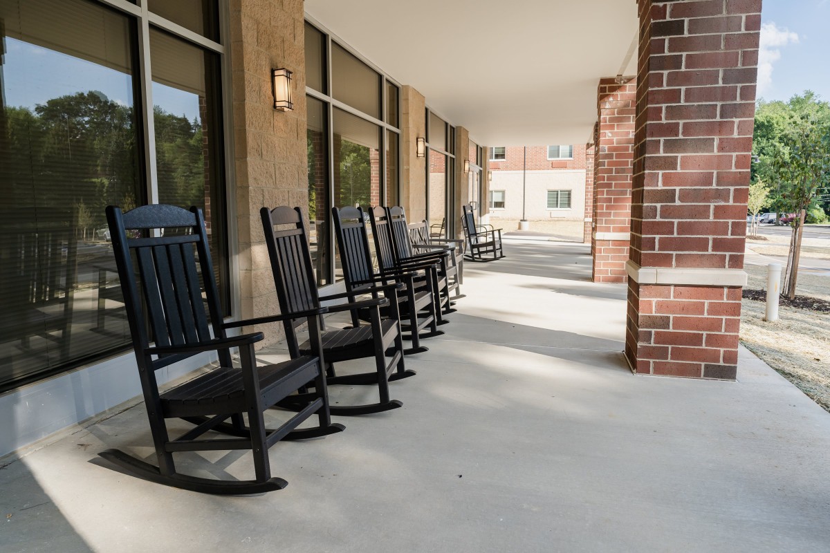 A row of black rocking chairs on a porch with brick and glass walls.