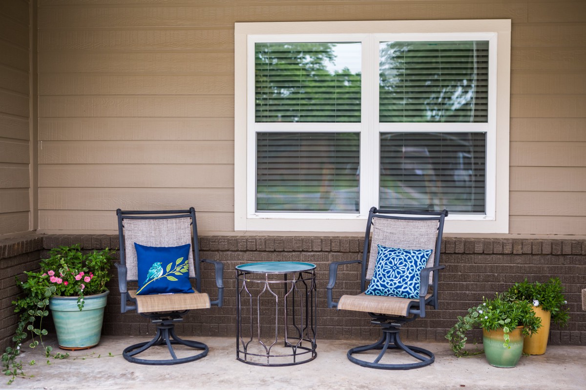A cozy outdoor patio setup with two chairs, a small table, and decorative cushions.