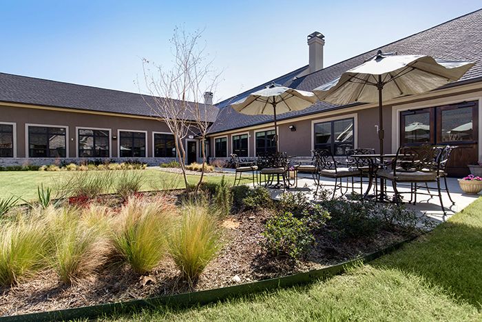 A modern building with a landscaped outdoor patio featuring tables and chairs under umbrellas.