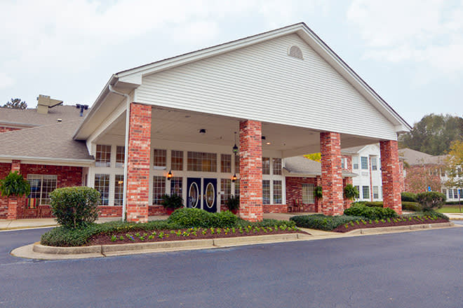 A brick building with an entrance supported by columns and surrounded by landscaping.