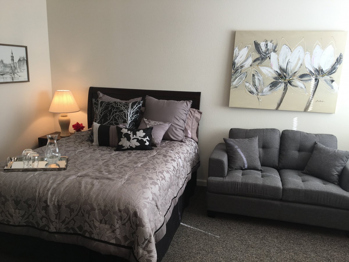 A cozy bedroom with a bed, a small couch, and soft lighting from a lamp, adorned with wall art.