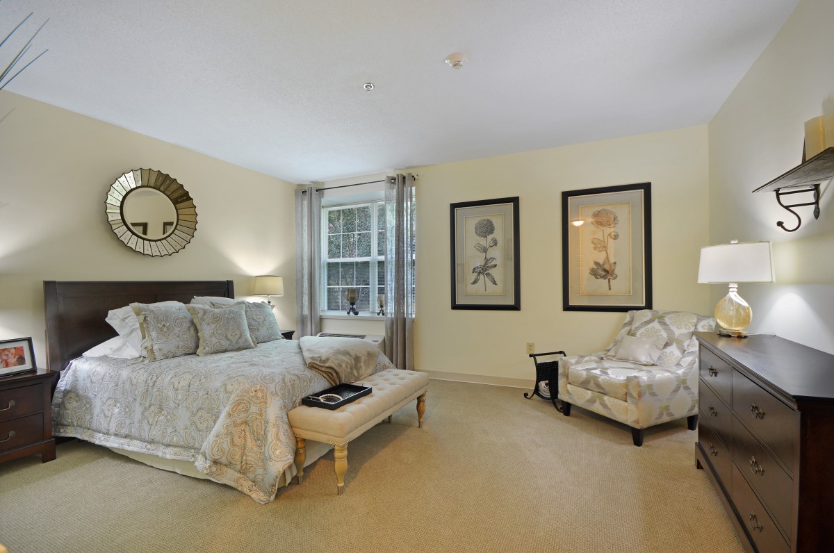 A spacious bedroom with elegant decor, featuring a large bed, an armchair, and framed artwork on the walls.