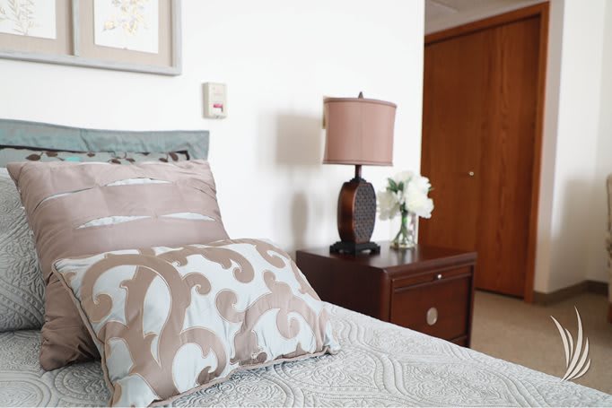 A cozy bedroom with decorative pillows and a lamp on the nightstand.