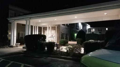 A well-lit entrance of a building at night surrounded by neatly trimmed hedges.