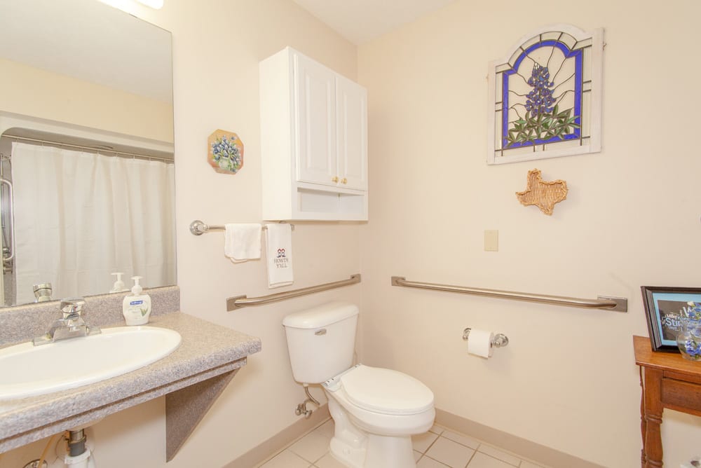 A bathroom with a toilet, sink, and handrails. The room features wall decor and a storage cabinet.