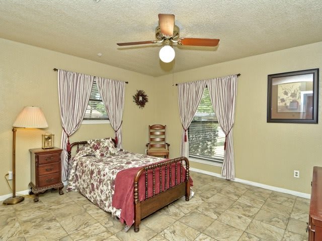 A cozy bedroom with a single bed, ceiling fan, and patterned curtains over the windows.