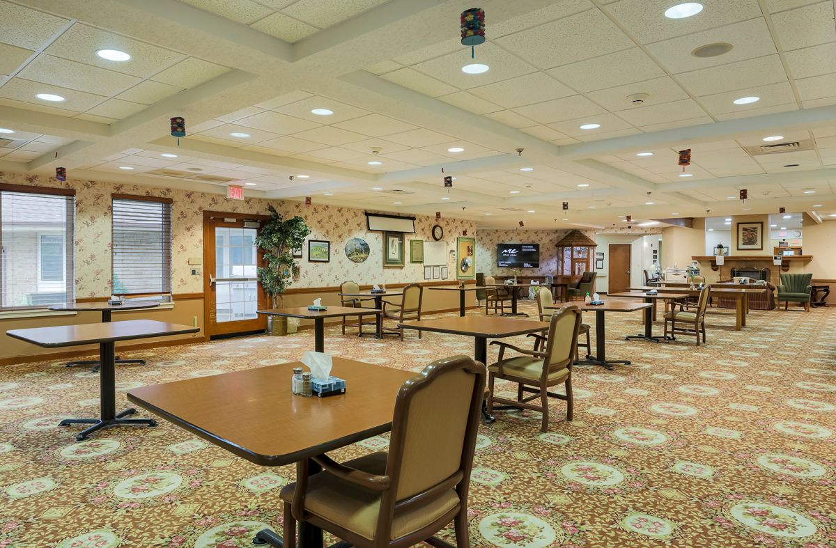 A spacious indoor dining area with several tables and chairs, decorative wall art, and carpeted flooring.