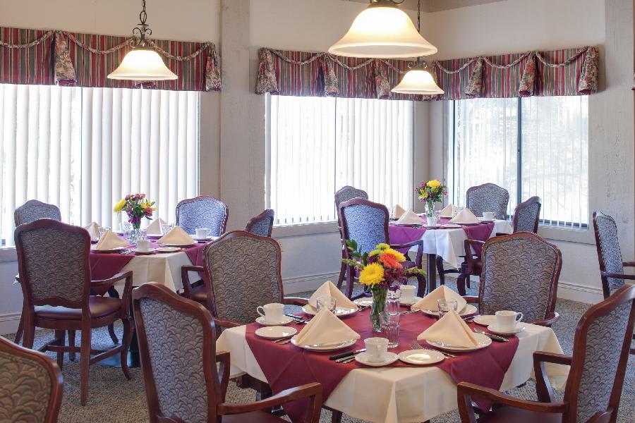 Elegant dining room with tables set for a meal, featuring flowers and folded napkins.