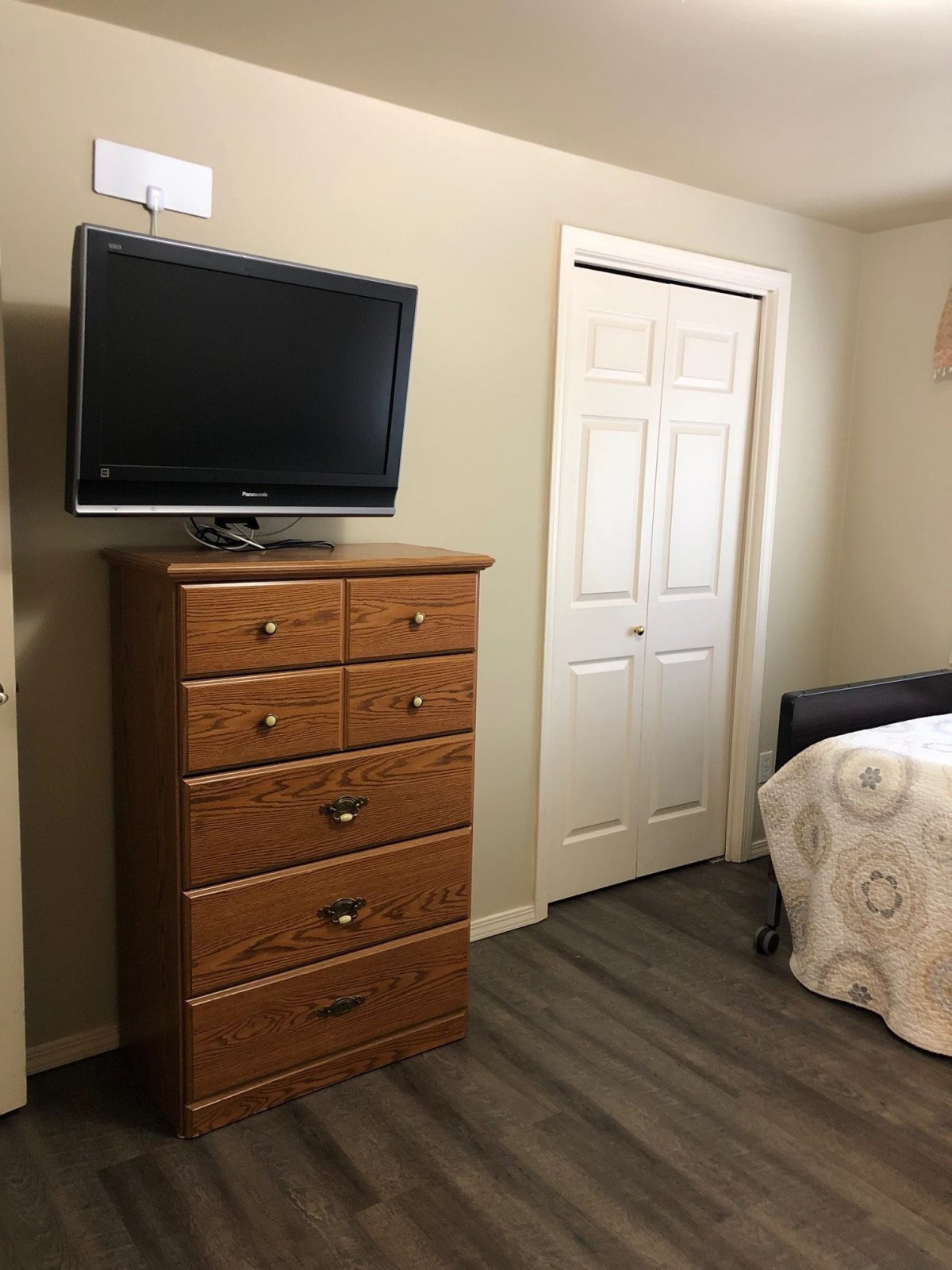 A simple bedroom with a wooden dresser, a mounted TV, and a bed.