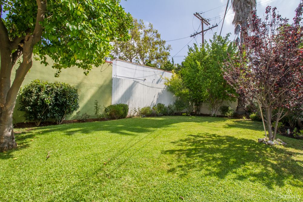A well-maintained grassy lawn bordered by trees and shrubs under a clear sky.