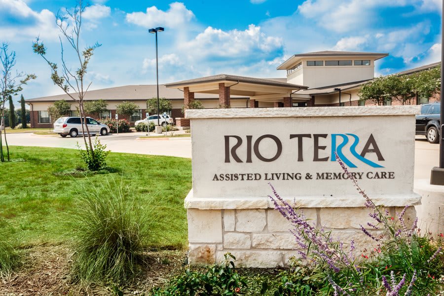 The entrance sign for Rio Terra Assisted Living and Memory Care against a backdrop of the building and landscaped grounds.