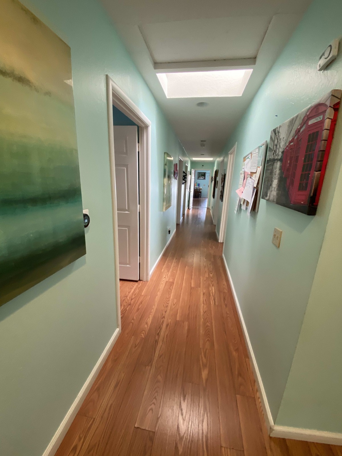 A long hallway with artworks on the walls and a wooden floor, illuminated by overhead lighting.
