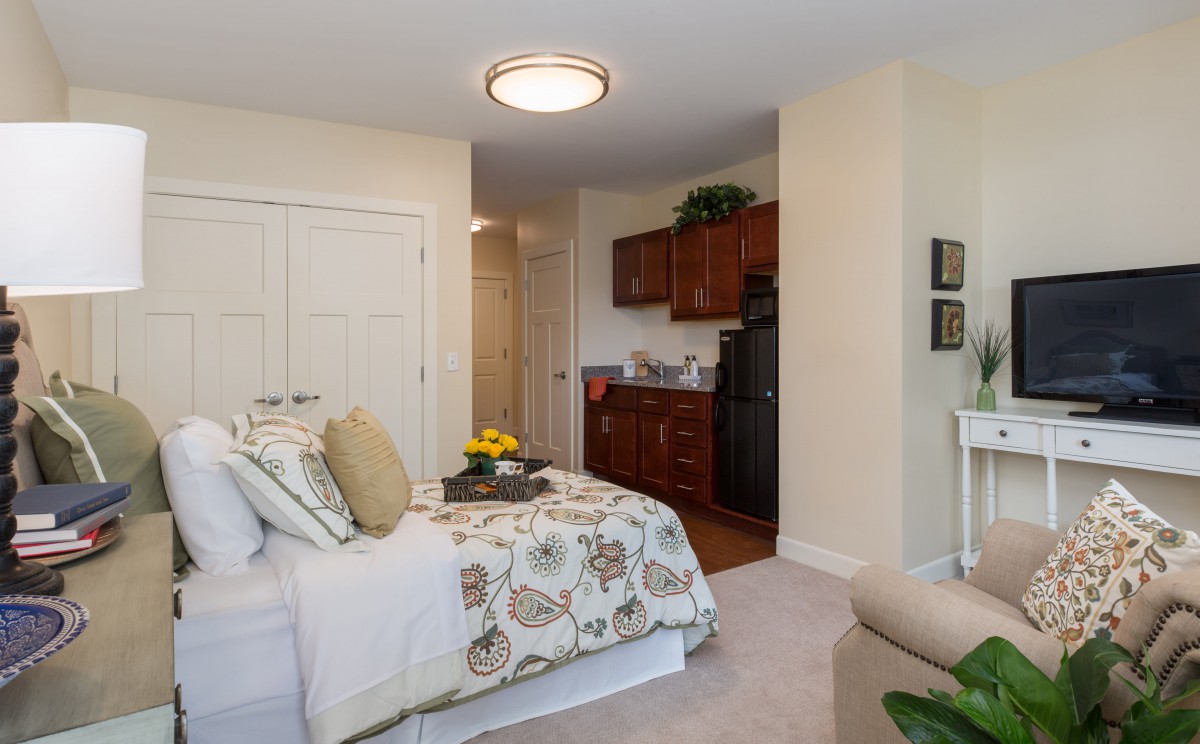A cozy bedroom with a kitchenette, featuring elegant decor and comfortable furnishings.