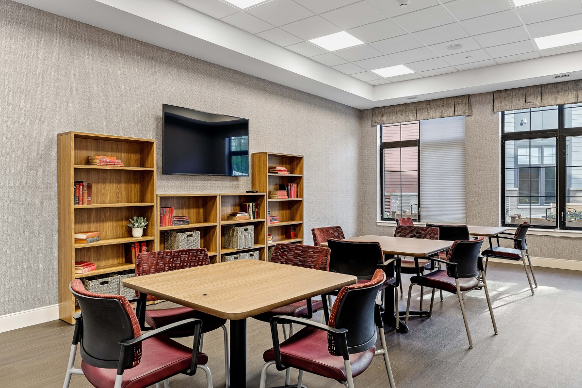 A study room with tables, chairs, and bookshelves, featuring a television and large windows.