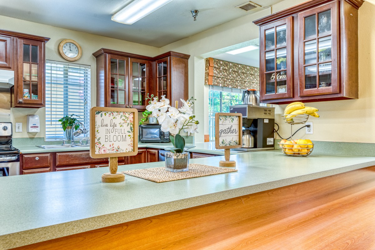 A bright and modern kitchen with wooden cabinetry, a central countertop adorned with flowers, and various appliances.