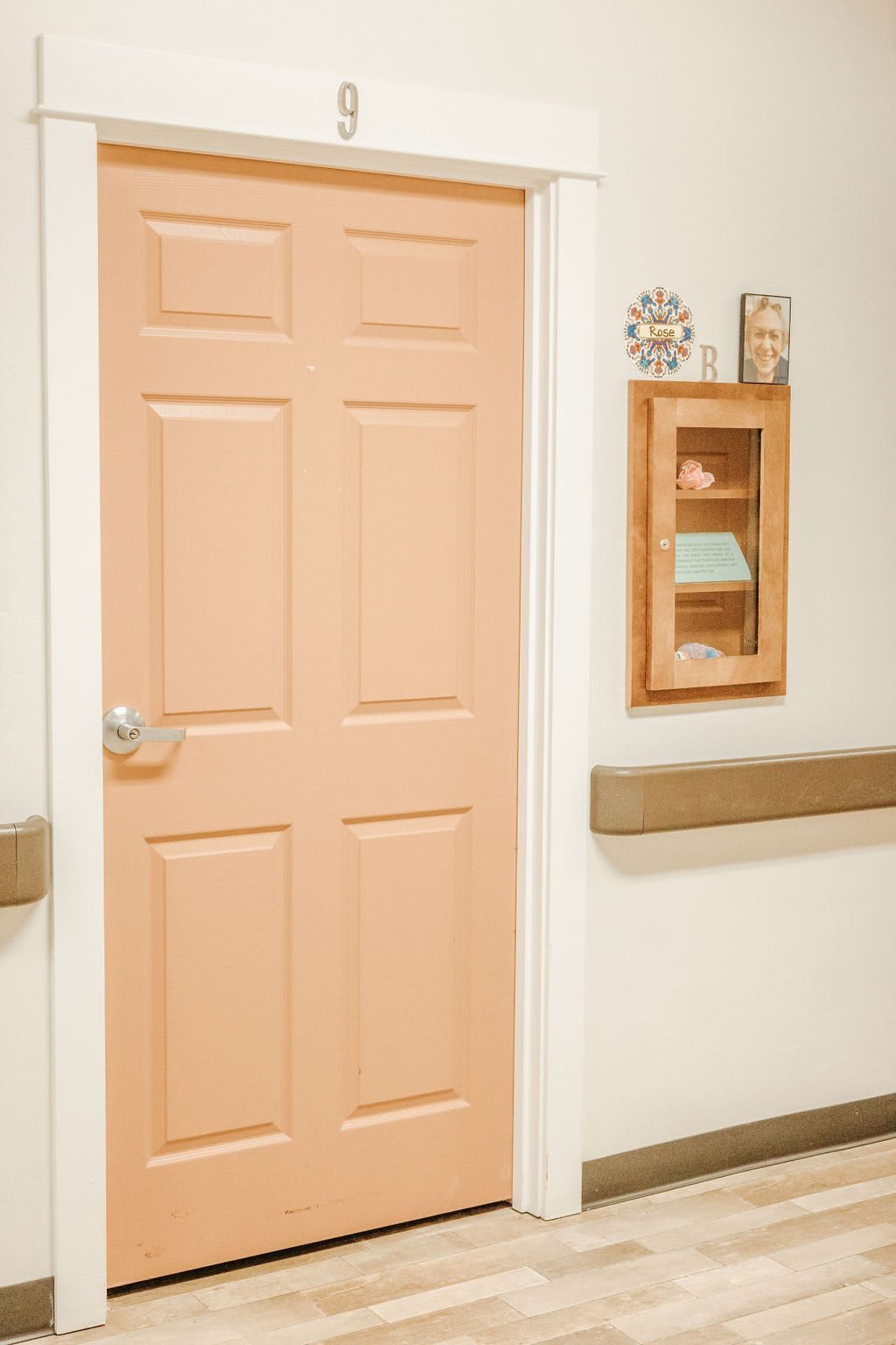 A peach-colored door in a hallway with a wooden cabinet hanging on the wall.