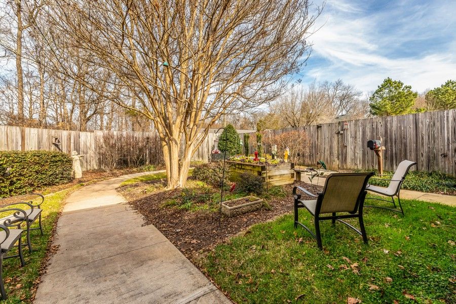 A tranquil garden area featuring a bench, pathway, and trees surrounded by a wooden fence.