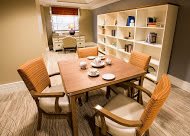 A cozy dining area with a wooden table surrounded by four chairs, complemented by bookshelves and a desk near the window.