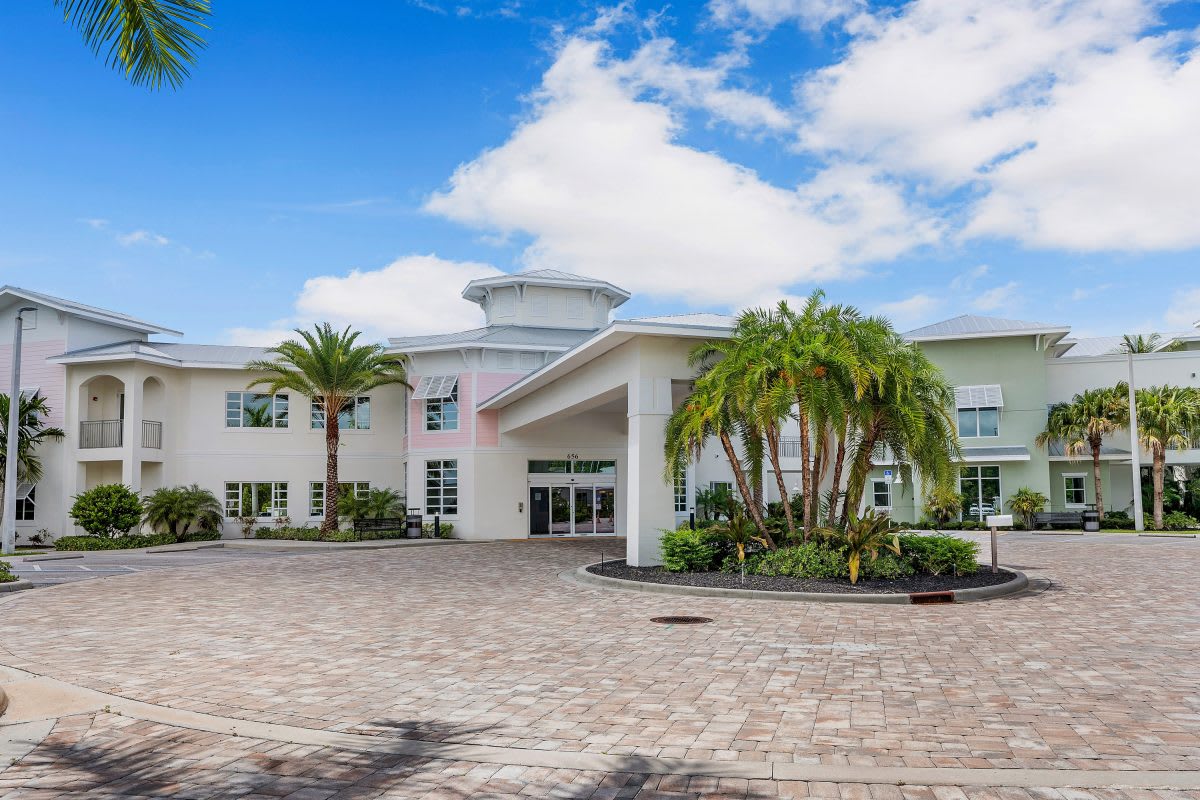 A modern building with palm trees under a blue sky with clouds.