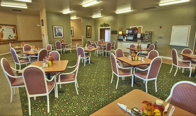 An empty cafeteria with neatly arranged tables and chairs, featuring a carpeted floor and soft lighting.