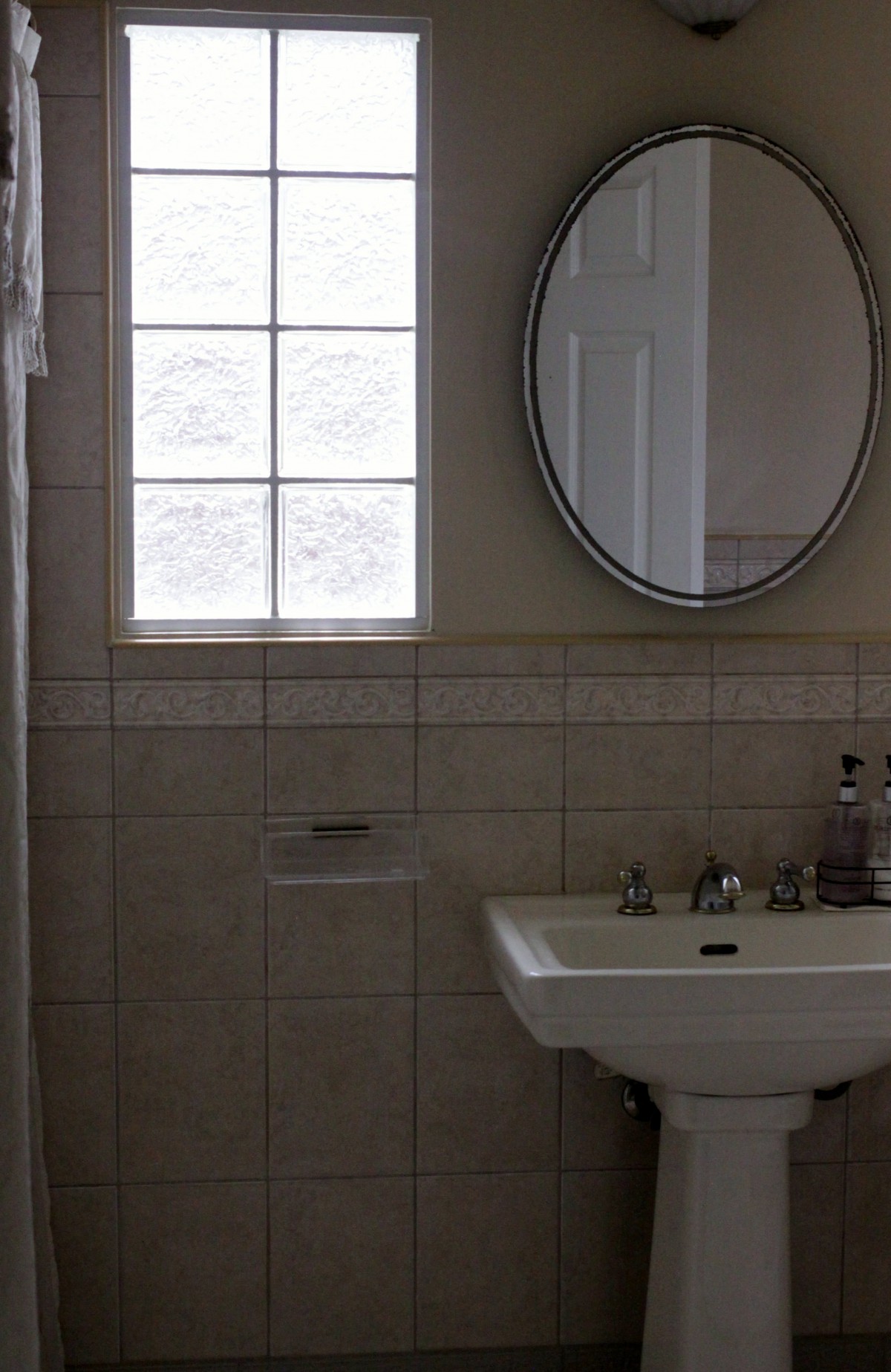A bathroom with a pedestal sink, round mirror, and tiled walls.