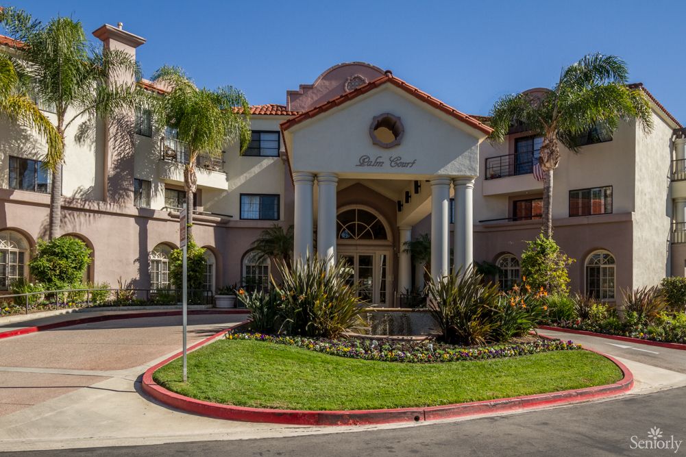 A beautiful building entrance surrounded by landscaped greenery and palm trees under a clear blue sky.
