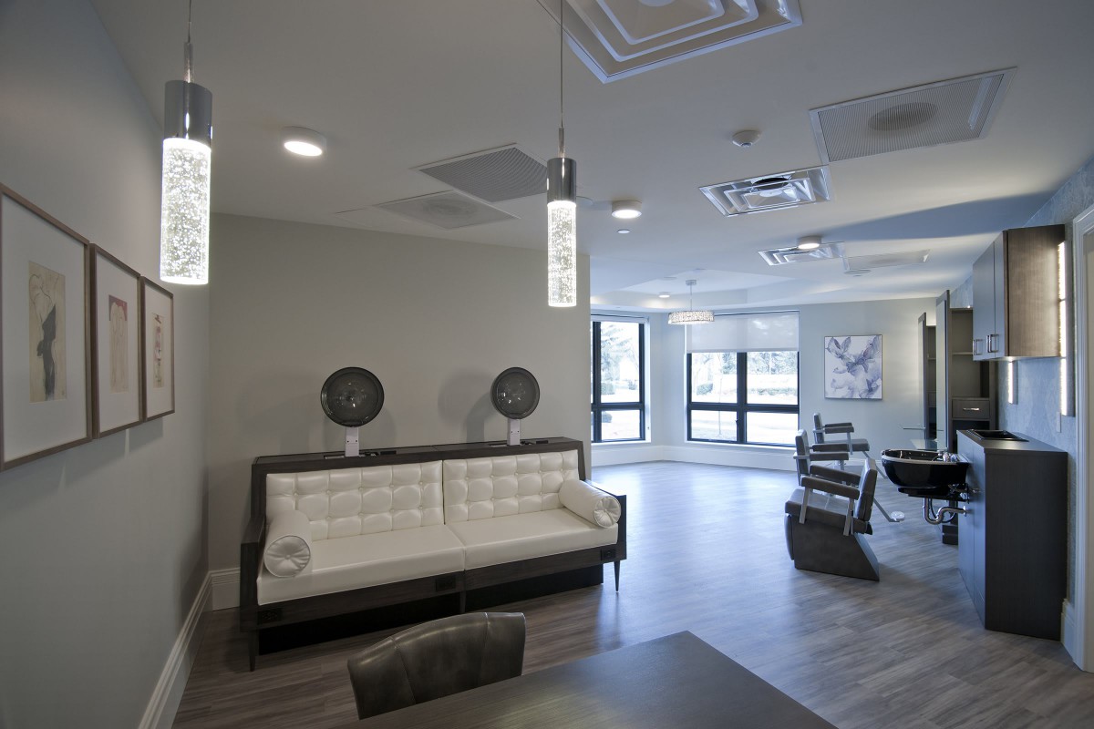 A modern salon interior with stylish lighting, comfortable seating, and workstations equipped with mirrors.