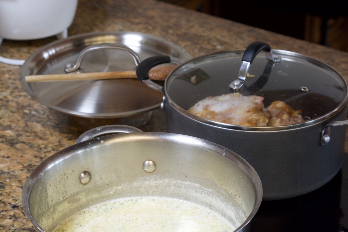 Two pots on a stovetop, one with a creamy liquid and the other with boiling contents, suggesting active cooking in a kitchen.