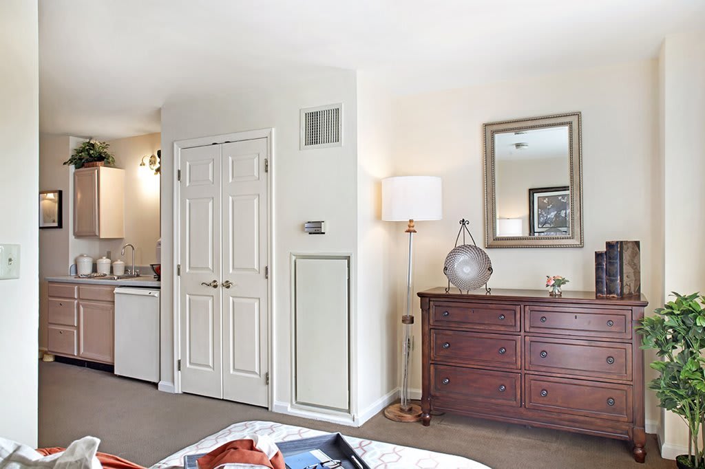 A cozy bedroom with a wooden dresser, lamp, and a mirror on the wall.