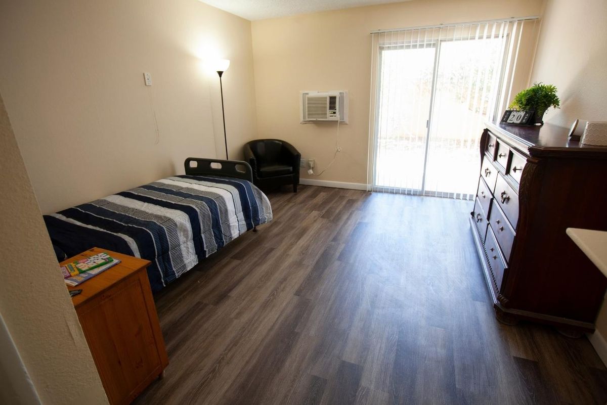A minimalist bedroom with a single bed, dresser, and chair.