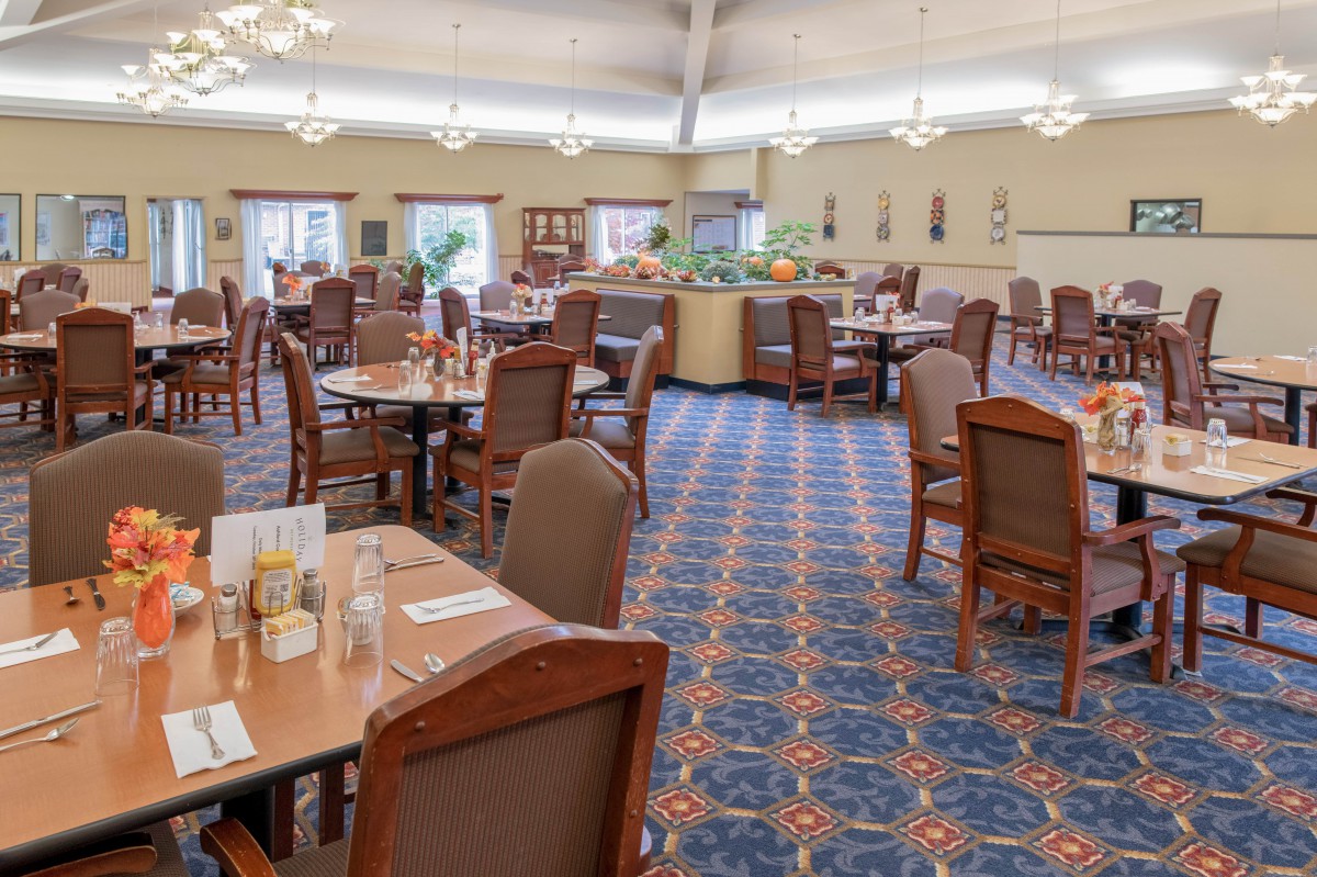 Spacious dining room with neatly arranged tables and chairs, featuring a patterned carpet and soft lighting.