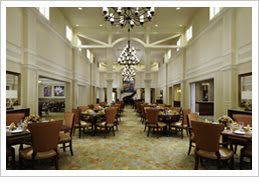 A spacious dining hall with neatly arranged tables and chairs, illuminated by elegant chandeliers.
