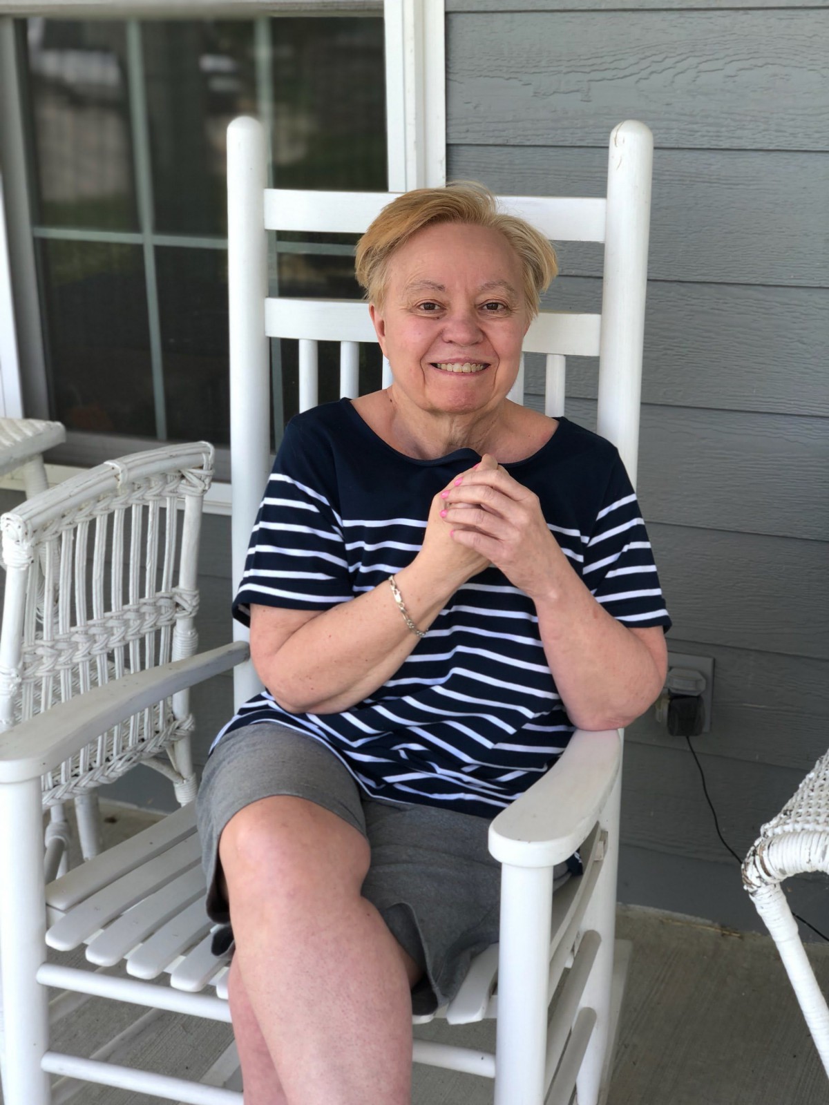 A woman sitting on a porch in a rocking chair, wearing a striped shirt and shorts.