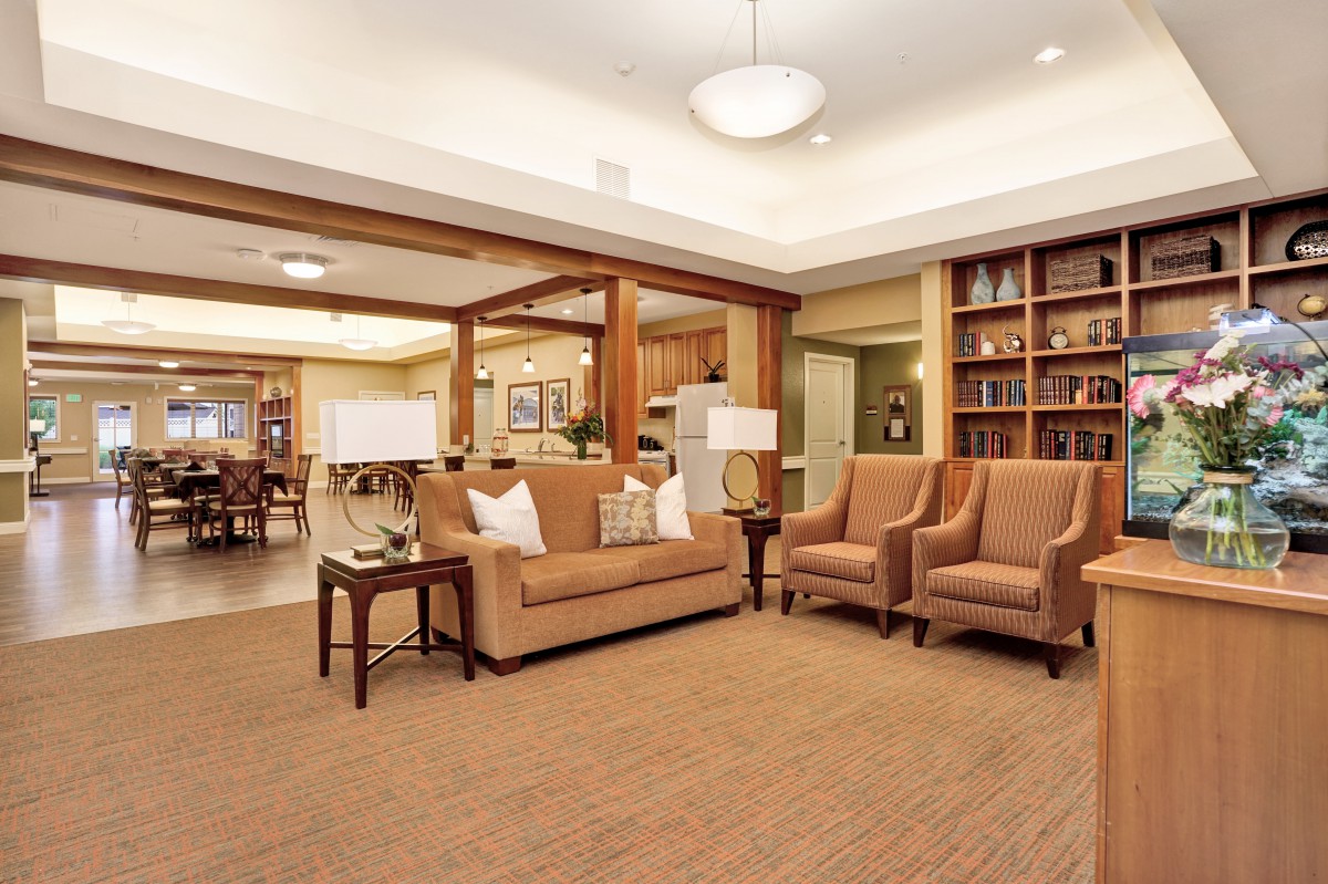 A spacious, well-lit living room with comfortable seating and a bookshelf.