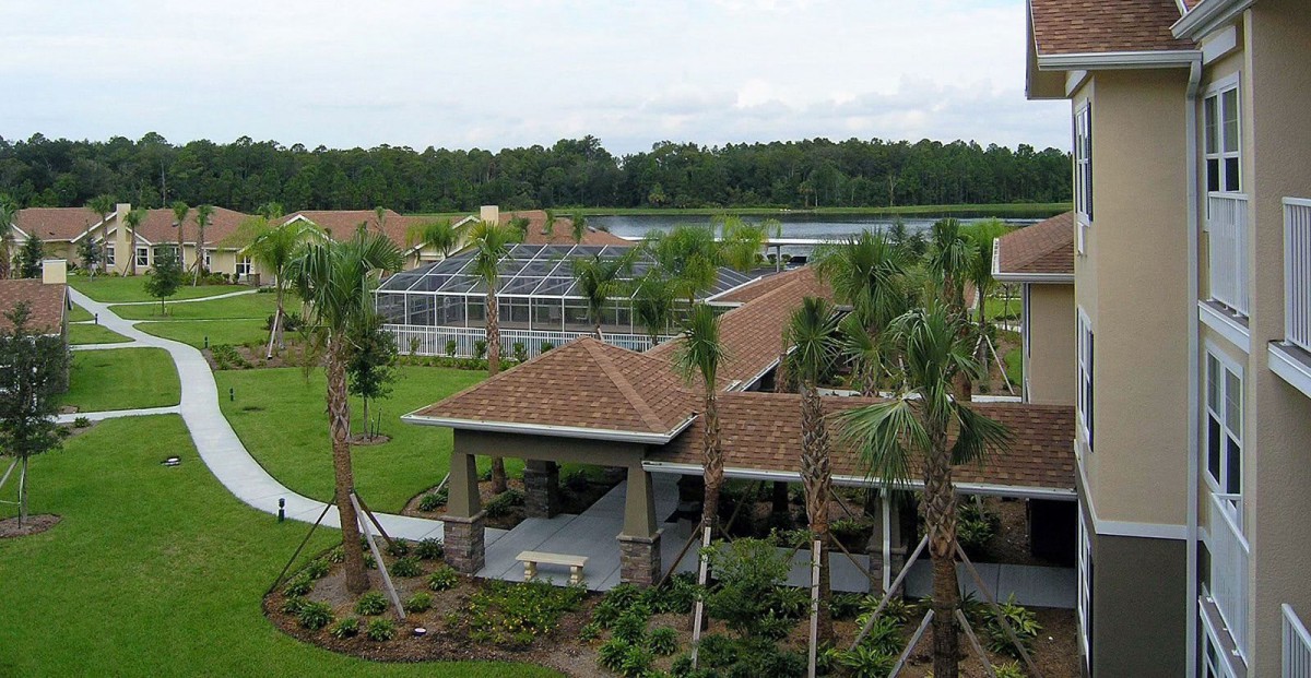 A tropical landscape featuring a greenhouse and a building surrounded by lush greenery and palm trees.