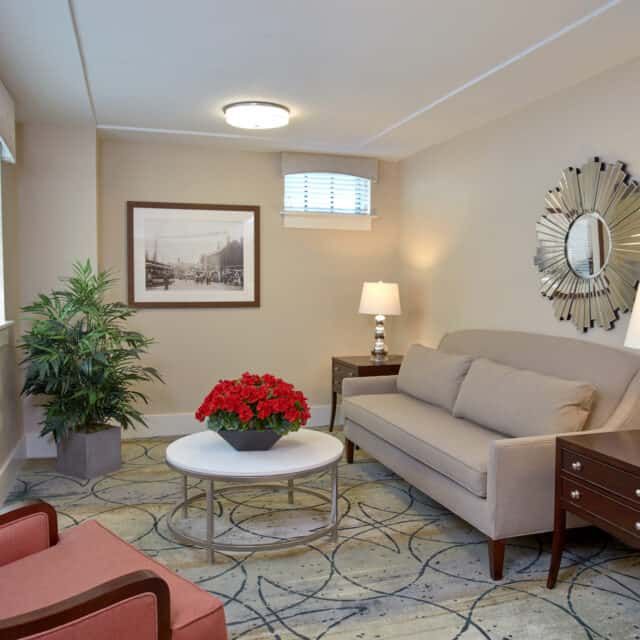 A cozy living room with a comfortable sofa, coffee table, elegant lamp, and decorative elements including artwork and plants.