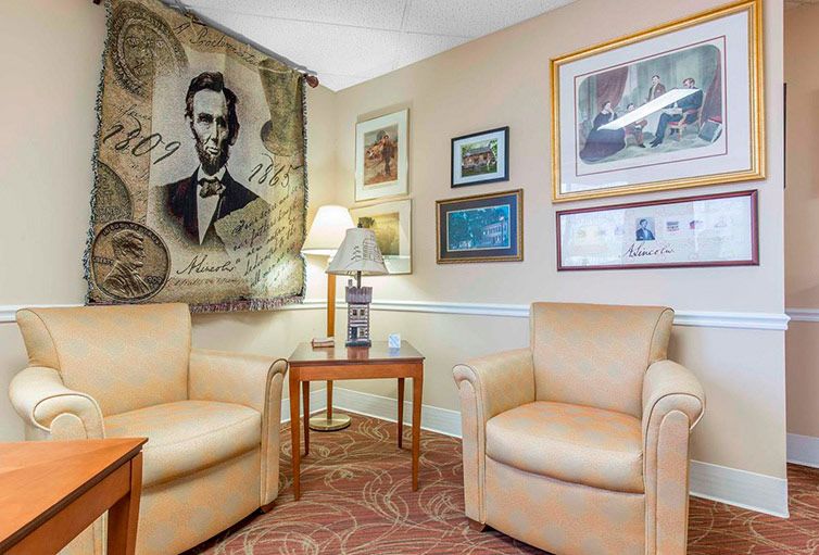 A cozy lounge area featuring two armchairs, a side table with a lamp, and various framed artworks adorning the walls.